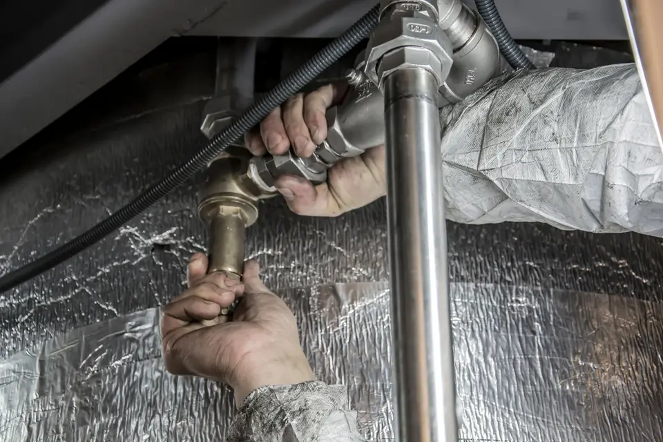 Hands tightening a pipe fitting under a sink
